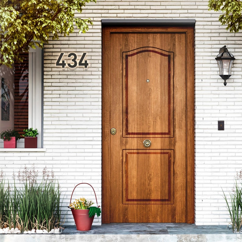 May include: A wooden front door with a decorative design and a brass doorknob. The number "434" is displayed above the door. A red bucket with flowers sits on the porch. A black lantern hangs on the wall.