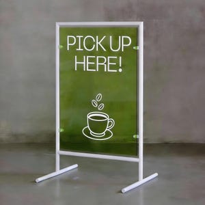 May include: A white metal sign with a green background. The sign reads "PICK UP HERE!" in white text, with a white coffee cup and coffee bean graphic. The sign is supported by a white metal frame and base.