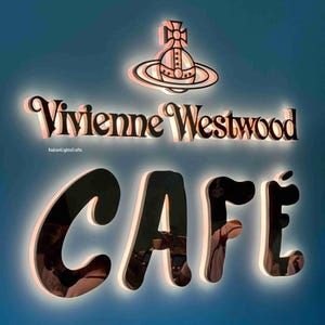 May include: A black and white sign with the text "Vivienne Westwood Cafe" in a bold, stylized font. The sign features a stylized orb logo with a cross on top, surrounded by a circle.