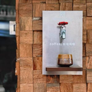 Puede incluir: Una estación de café con un grifo plateado y un mango rojo, montada en una placa de metal. La placa tiene el texto "MIFUN STUDIO" y "coffee / 有啥喝啥". Una pequeña taza marrón y dorada se encuentra en un estante de madera.