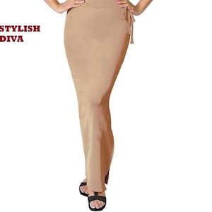 Puede incluir: Una falda beige ajustada con un detalle de lazo en la cintura. La falda es larga y llega hasta los tobillos. El texto "STYLISH DIVA" está impreso en rojo en la esquina superior izquierda. La persona lleva sandalias negras.