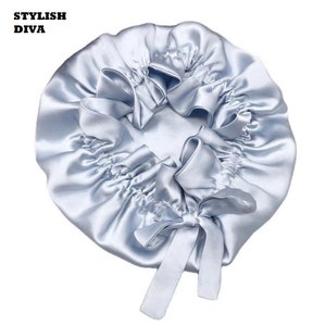 May include: A light blue satin bonnet with a gathered design and a bow. The text "STYLISH DIVA" is printed in black at the top left. This bonnet is designed to protect hair while sleeping.