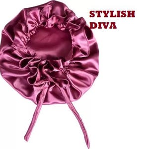 May include: A satin bonnet in a deep rose color, with a ruffled edge and long ties. The text "STYLISH DIVA" is printed in red. This hair accessory is designed to protect and style hair.