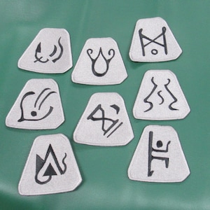 May include: Nine white fabric patches with black embroidered symbols. The symbols are abstract and geometric.