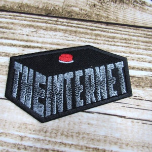Peut inclure: Un patch brodé noir avec un bouton rouge sur le dessus. Le texte "THE INTERNET" est brodé en blanc sur le patch.