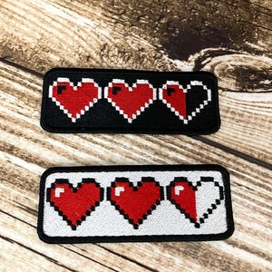 May include: Two rectangular patches featuring pixelated red hearts. One patch has a black background, the other has a white background. Each patch shows three hearts, with the last heart partially empty, representing health or life.