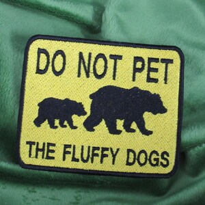 Peut inclure: Patch brodé jaune et noir avec le texte "Do Not Pet The Fluffy Dogs" et une silhouette de deux ours.