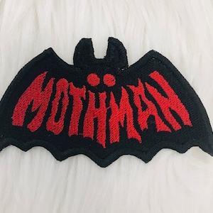 May include: Black bat-shaped patch with red embroidered text that reads "MOTHMAN".