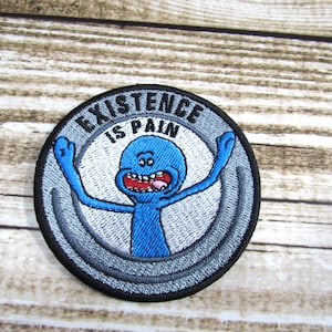 May include: A round, black and gray embroidered patch with a blue alien character with a wide open mouth and outstretched arms. The text "EXISTENCE IS PAIN" is written in black around the alien character.