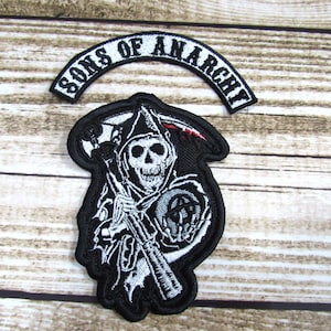 May include: Two embroidered patches, one with the text "Sons of Anarchy" in a white arc and the other with a black and white image of a grim reaper holding a scythe and a skull.