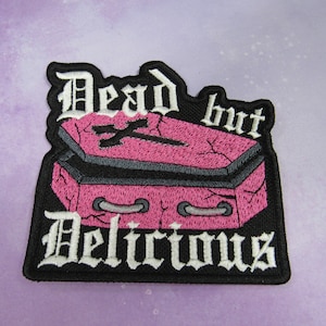 May include: Black and white embroidered patch with a pink coffin and the text "Dead but Delicious".