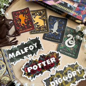 May include: Four colorful stickers featuring the Hogwarts house crests: Gryffindor, Hufflepuff, Ravenclaw, and Slytherin.  Three additional stickers feature the names "Malfoy", "Potter", and "Diggory" with floral designs.