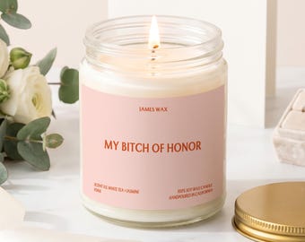 May include: A clear glass jar candle with a lit wick and a light pink label. The label features the text "JAMES WAX", "MY BITCH OF HONOR", "SCENT 03 WHITE TEA + JASMINE", "F068", and "100% SOY WAX CANDLE HANDPOURED IN CALIFORNIA" in dark orange text.