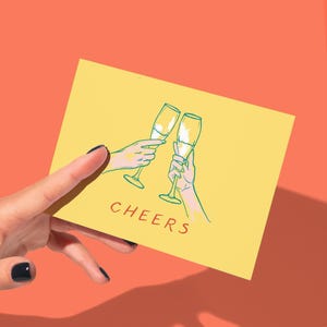 May include: A yellow greeting card with the word "CHEERS" in red. The card features a green and white illustration of two hands toasting champagne flutes. The background is a solid orange color.