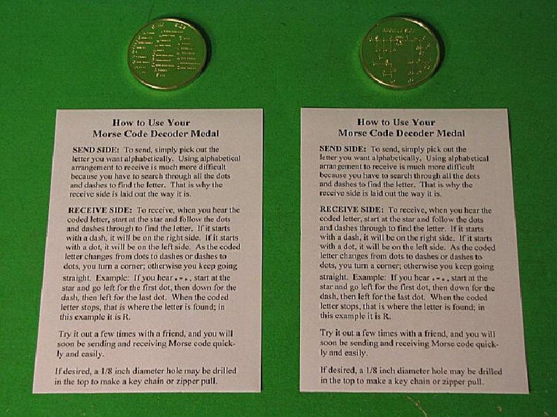 May include: Two white cards with instructions on how to use a Morse code decoder medal. The cards are on a green background. The medal is a gold-colored disc with a star in the center and dots and dashes around the star. The text on the cards explains how to send and receive Morse code using the medal. The text also mentions that a 1/8 inch diameter hole can be drilled in the top of the medal to make a key chain or zipper pull.