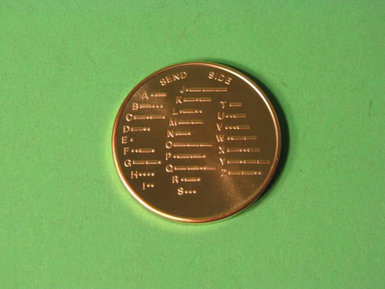 May include: A gold-colored metal token with the letters A through Z and their corresponding Morse code representations. The token is labeled "SEND SIDE" at the top.
