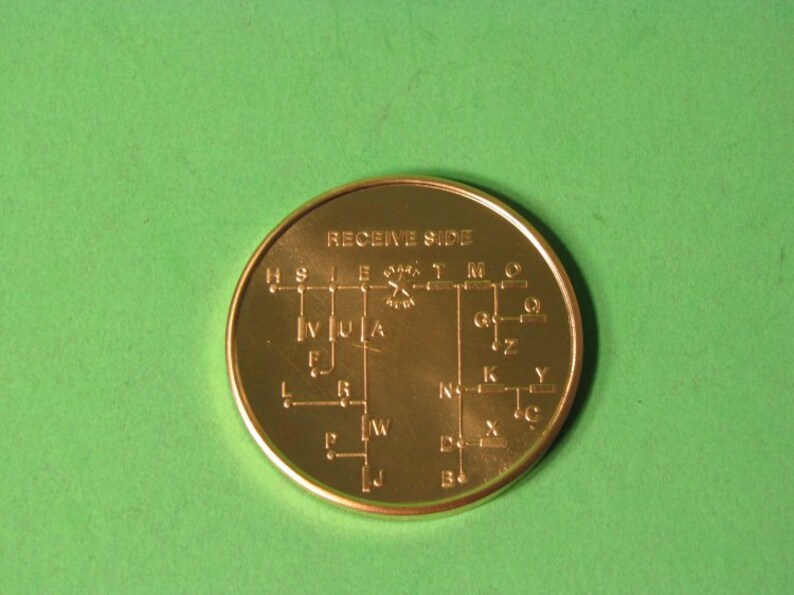 May include: A gold-colored metal token with the words "RECEIVE SIDE" printed on it. The token has a diagram of a circuit board with letters and numbers printed on it.