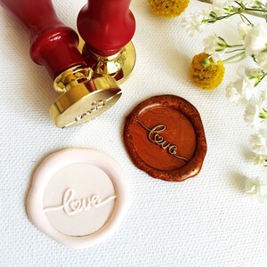 May include: Two gold wax seals with the word "love" written in cursive on them. One seal is pink and the other is brown.