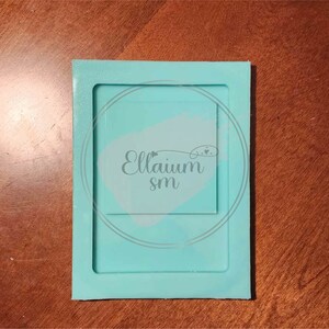 May include: A light blue silicone mould with a square cutout. The mould is designed for creating resin crafts. The mould has the text "Ellaium sm" printed on it.