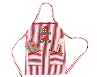 Puede incluir: Delantal a rayas rojas y blancas con un diseño de hombre de jengibre. El delantal tiene dos bolsillos y una aplicación de hombre de jengibre con la palabra "Name" bordada. Una pequeña galleta de jengibre está en un bolsillo.