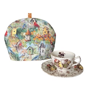 May include: A tea set featuring a birdhouse-themed tea cozy and a teacup with saucer. The cozy has a colorful bird and birdhouse pattern. The teacup and saucer have a fruit design.