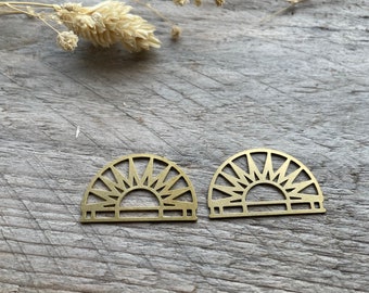 May include: Two gold metal sunburst earrings with a geometric design. The earrings are on a wooden surface.