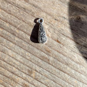 May include: A silver teardrop-shaped pendant with an intricate floral design.