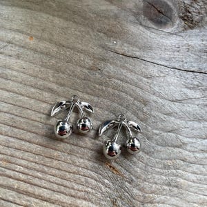 Peut inclure: Deux pendentifs en argent en forme de cerises avec des tiges et des feuilles.