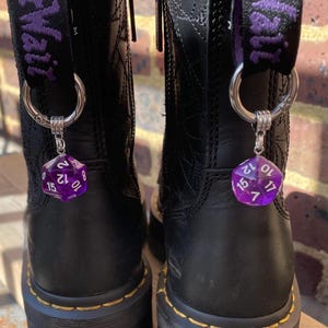以下が含まれることがあります： 紫色のストラップと紫色のd20ダイスチャームがそれぞれに付いた、黒い革のブーツのペアです。