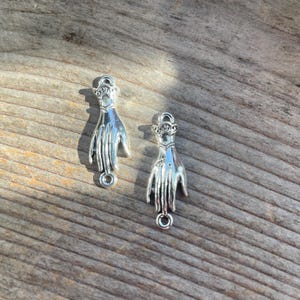 May include: Two silver hand charms with a detailed design. Each charm has a loop at the bottom for attaching to a necklace or bracelet.