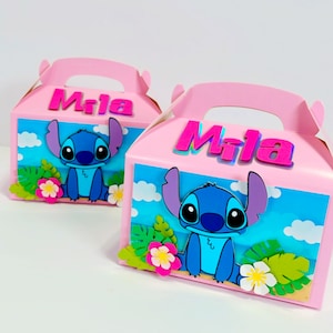 May include: Two pink favor boxes with a blue Stitch character from Lilo & Stitch. The boxes have a beach scene with clouds, palm leaves, and flowers. The name "Mila" is written on the front of each box in pink letters.