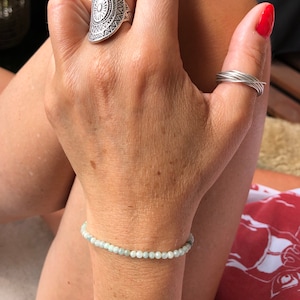 May include: A delicate bracelet made of light blue gemstone beads. The bracelet is on a person's wrist.