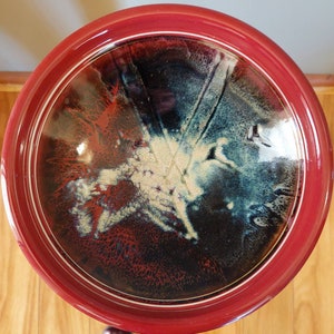 May include: A red ceramic bowl with a white rim and a black and white abstract design. The bowl has a glossy finish and a speckled texture.