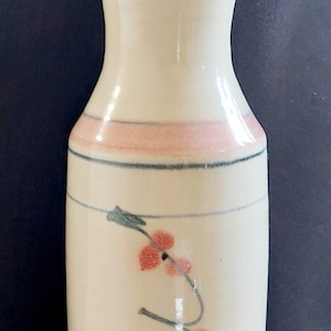 May include: Cream-coloured ceramic pitcher with a flared top and a small spout. The pitcher features a pink band and a floral design with red flowers and green stems. The design is hand-painted, giving it a unique, artisanal look.
