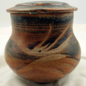 May include: A brown and black ceramic jar with a lid. The jar has a swirling pattern and a speckled glaze.