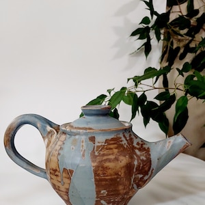 May include: A blue and brown ceramic teapot with a drip glaze. The teapot has a rounded body and a spout on the side.