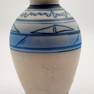 May include: A small, white ceramic vase with a blue and black geometric design. The vase has a rounded body and a narrow neck.