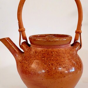 May include: A brown ceramic teapot with a speckled glaze and a woven bamboo handle.