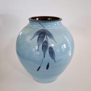 May include: A light blue ceramic vase with a dark brown rim and a hand-painted design of blue leaves.