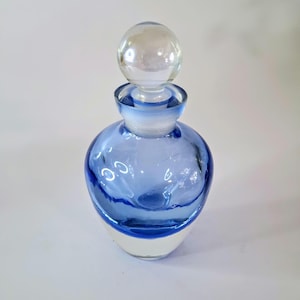 May include: A blue glass bottle with a clear glass stopper. The bottle has a rounded body and a clear base. The bottle is decorated with a blue swirl design.