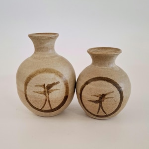May include: Two ceramic vases with a light brown glaze and a brown dragonfly design. The larger vase is taller and wider than the smaller vase.