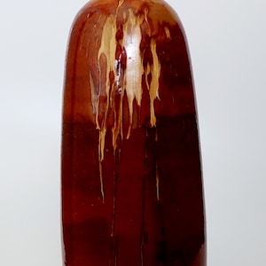 May include: A tall, brown ceramic vase with a narrow neck and a rounded body. The vase has a unique glaze that creates a mottled effect with streaks of light brown and yellow.