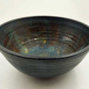 May include: A handcrafted ceramic bowl with a dark blue exterior and a textured finish. The interior showcases a mix of blue, brown, and yellow tones. The bowl has a wide, open design, ideal for serving or display purposes.