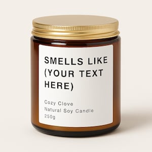 May include: A brown glass jar with a gold lid, displaying a white label with the text "SMELLS LIKE (YOUR TEXT HERE)". The label also reads "Cozy Clove, Natural Soy Candle, 250g".