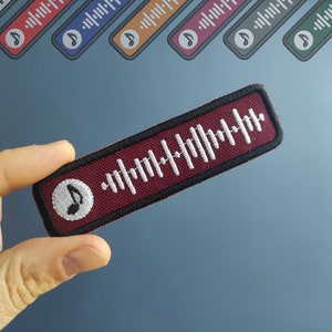 May include: A maroon fabric patch with a white musical note and a white barcode-like design. The patch has a black border.