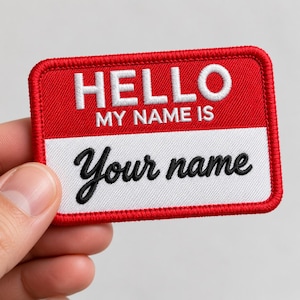 May include: A rectangular embroidered patch with a red border and a red top section featuring the white text HELLO MY NAME IS. The bottom section is white with the black cursive text Your name embroidered across the center of the patch.