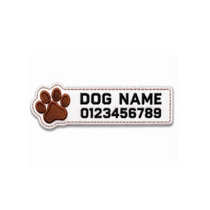 Op de afbeelding: Een rechthoekige witte geborduurde patch met een bruine pootafdruk aan de linkerkant. De tekst DOG NAME is in het zwart geborduurd op de bovenste regel en de cijfers 0123456789 in het zwart op de onderste regel, alles binnen een rand.