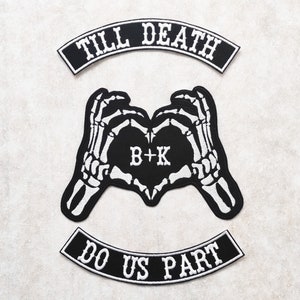 Może przedstawiać: Trzy haftowane łatki w kolorze czarnym i białym z tekstem "Till Death Do Us Part" i kształtem serca utworzonym przez dwie szkieletowe dłonie z inicjałami "B+K" wewnątrz serca.