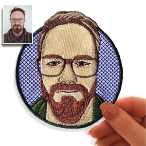 Peut inclure: Patch brodé représentant une personne aux cheveux bruns et à la barbe portant des lunettes. Le patch est rond et a un fond à carreaux bleu et blanc.