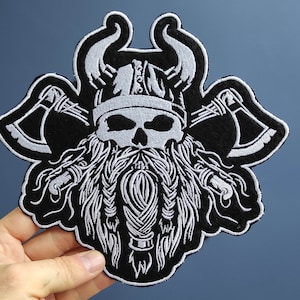 Könnte beinhalten: Schwarz-weiß gestickter Patch eines Schädels, der einen gehörnten Helm trägt und zwei Äxte hält. Der Schädel hat einen langen, geflochtenen Bart.